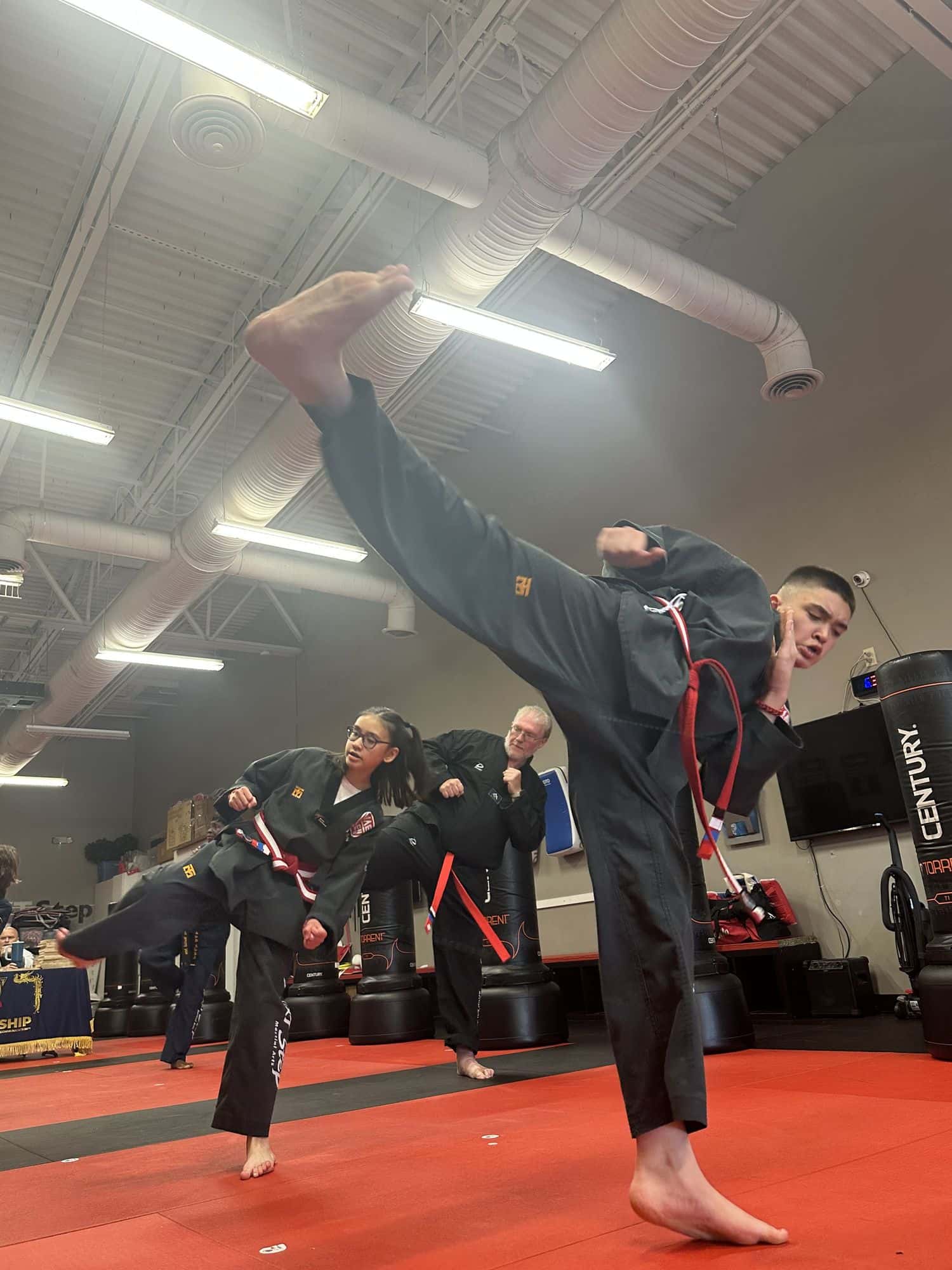 Teen and adult students throwing high kicks together on the red mats at NEXTStep Martial Arts in Gettysburg