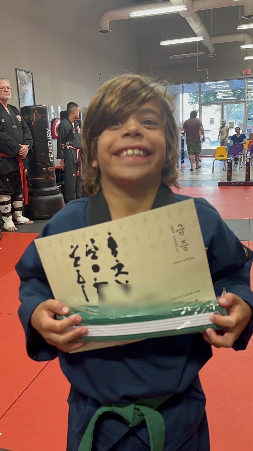 A grinning student holds his new belt and certificate