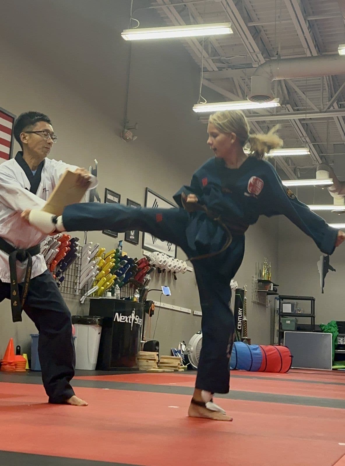 A Junior Warriors student side-kicking a board held by an instructor