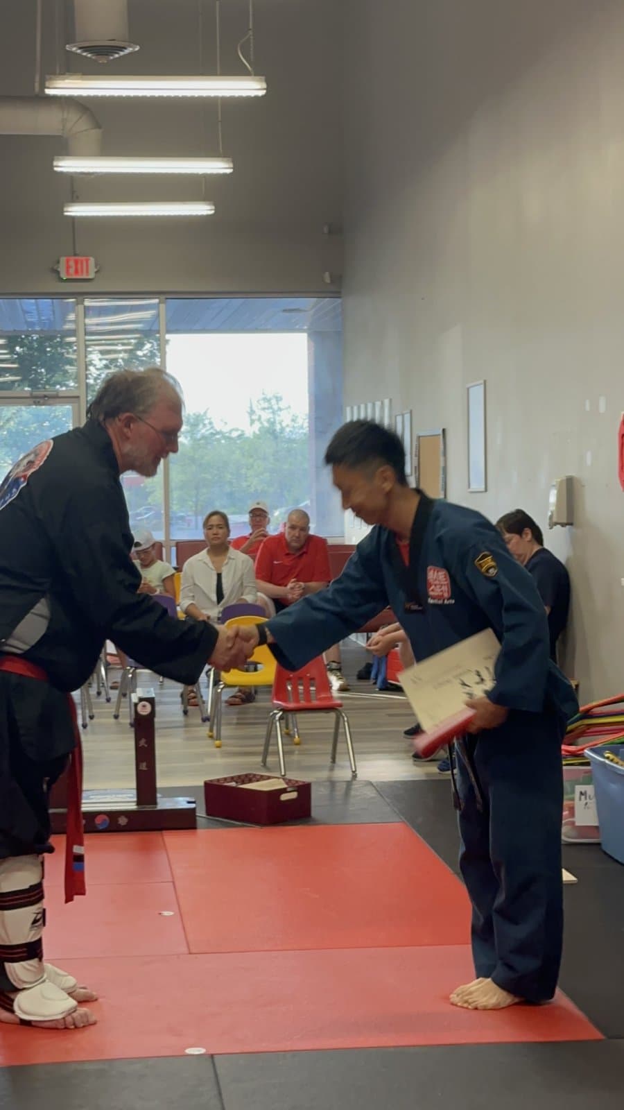 An adult student shaking hands with Master Jay after breaking his board at a belt test