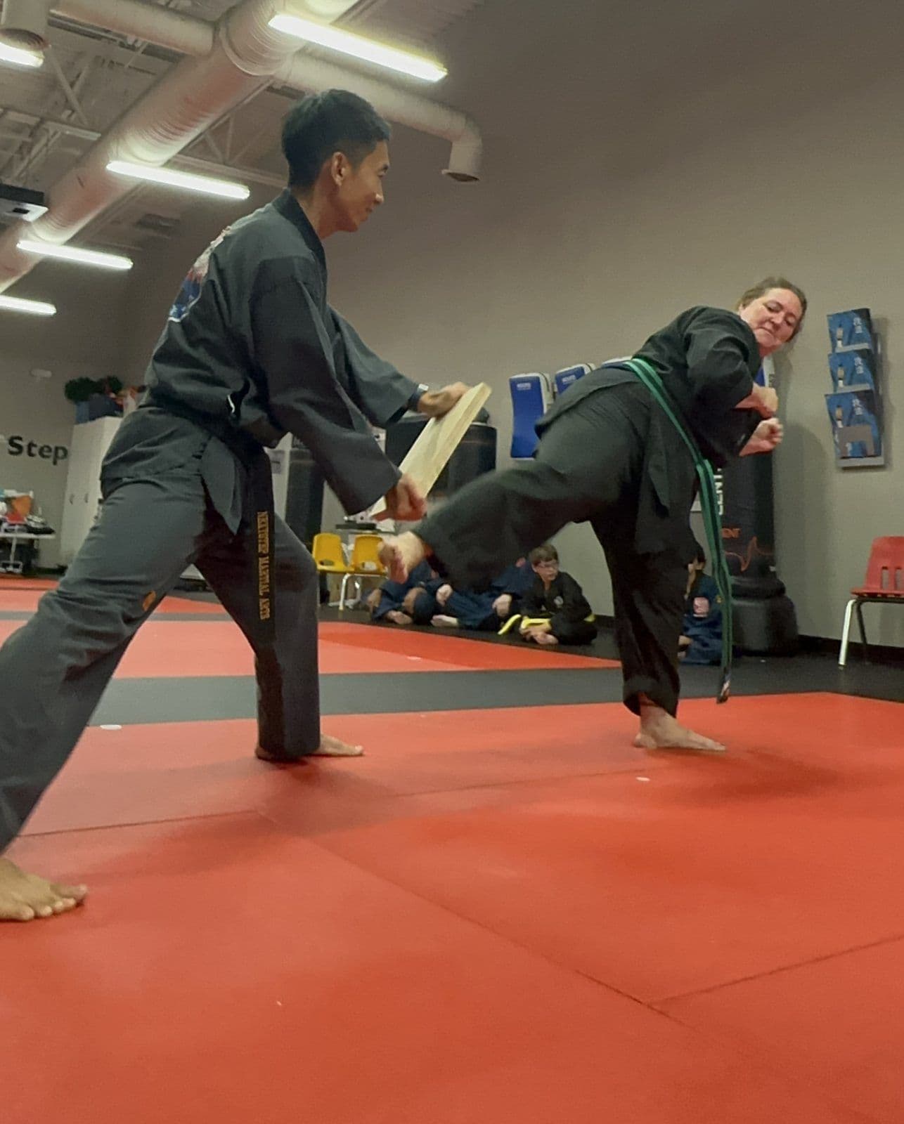 An adult student kicking a board held by an instructor