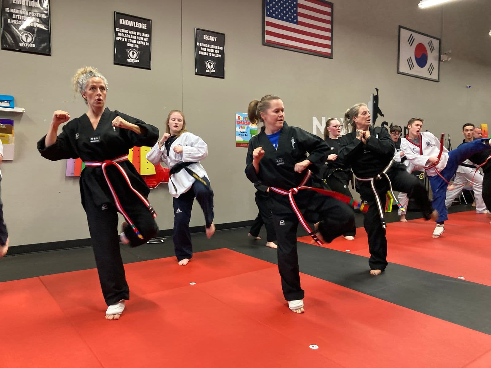 Adult and teen NEXTStep students practicing Taekwondo kicks together in uniform