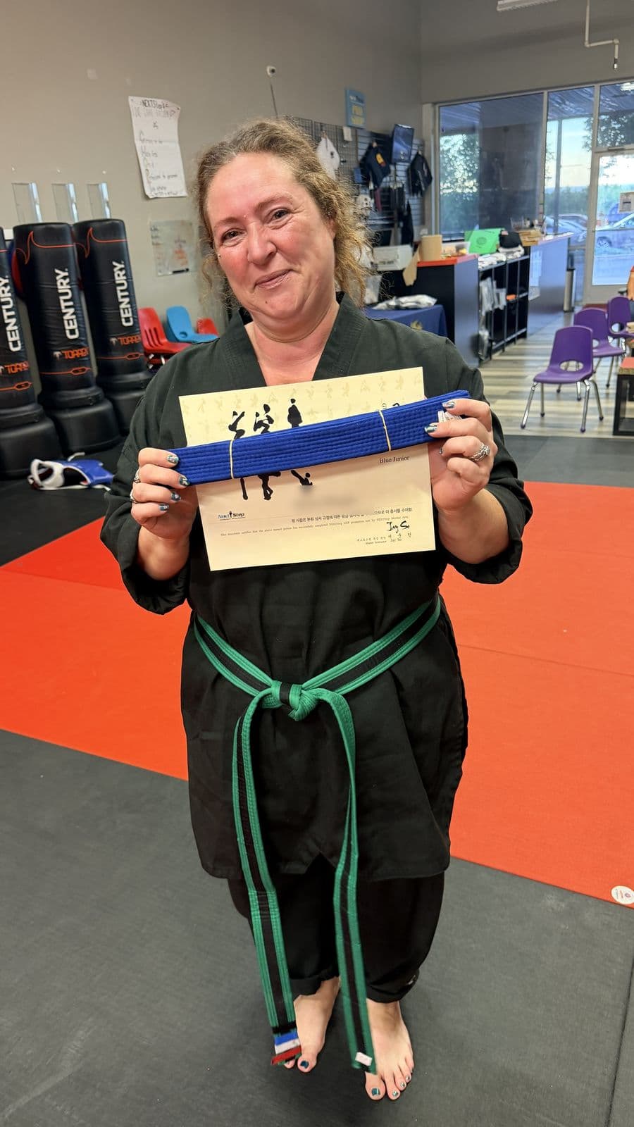 An adult student smiling with her new belt and certificate