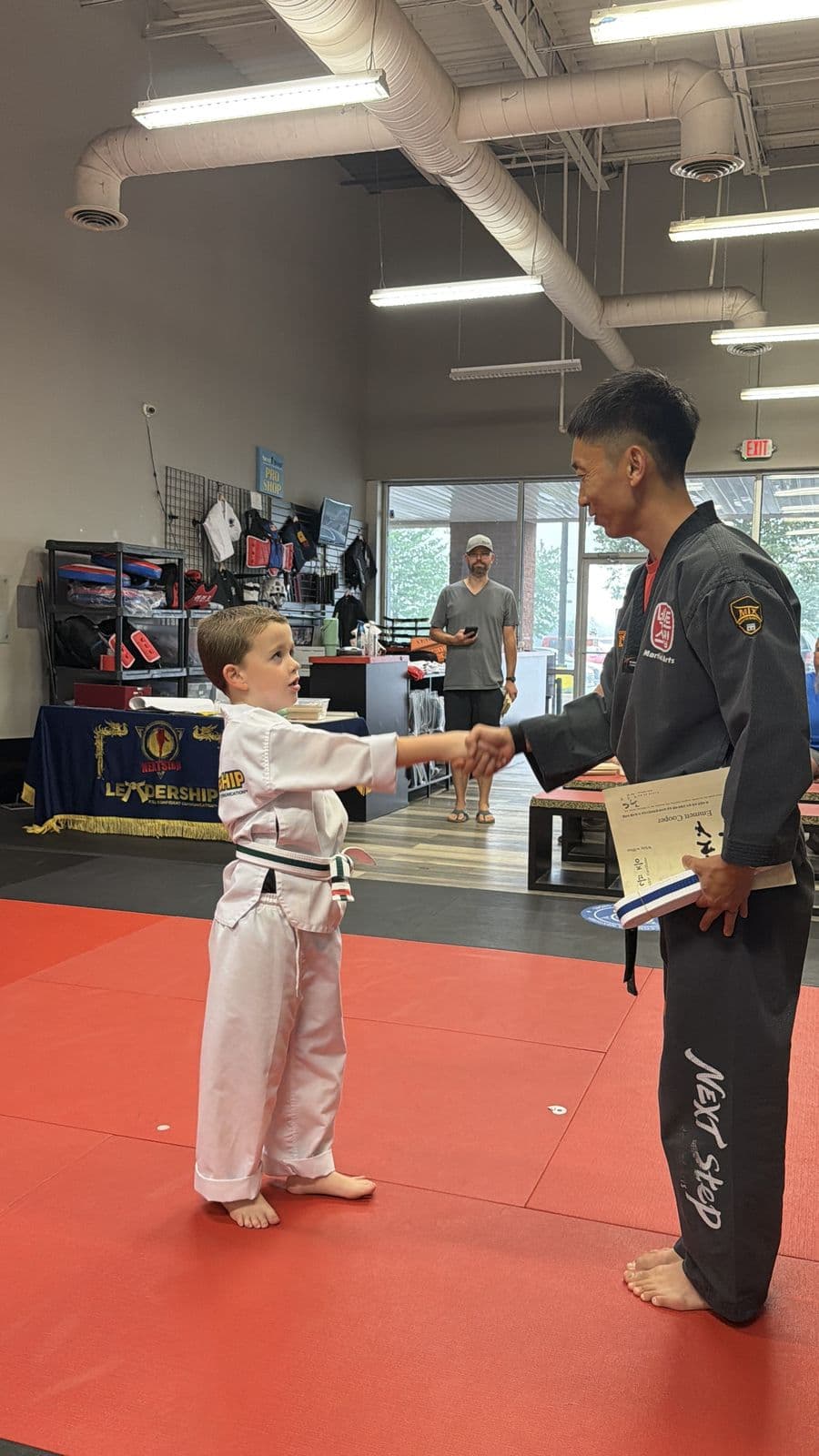 A young student shaking hands with his instructor at a belt ceremony