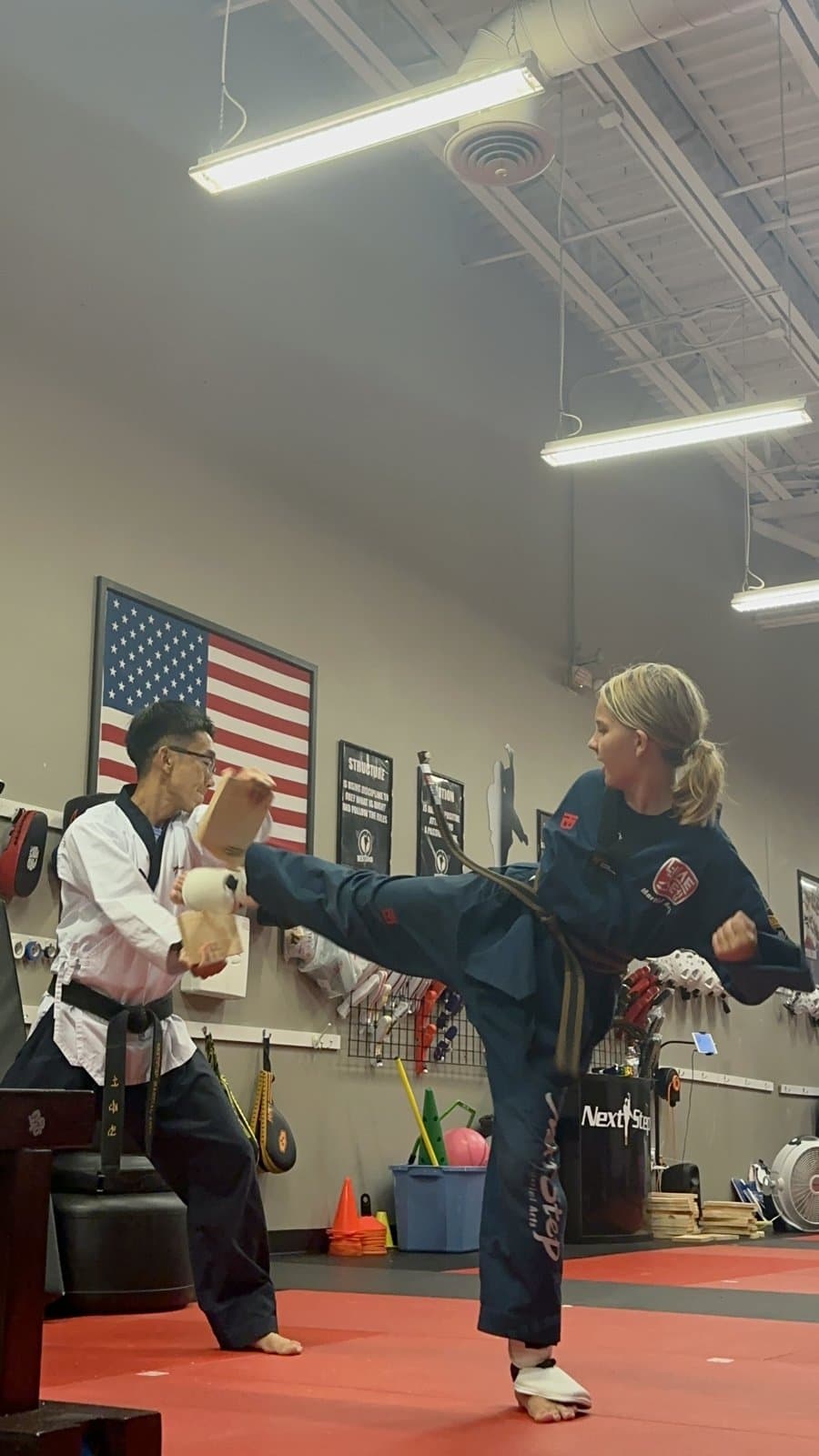 A student landing a kick on a board held by Master Jay during a belt test