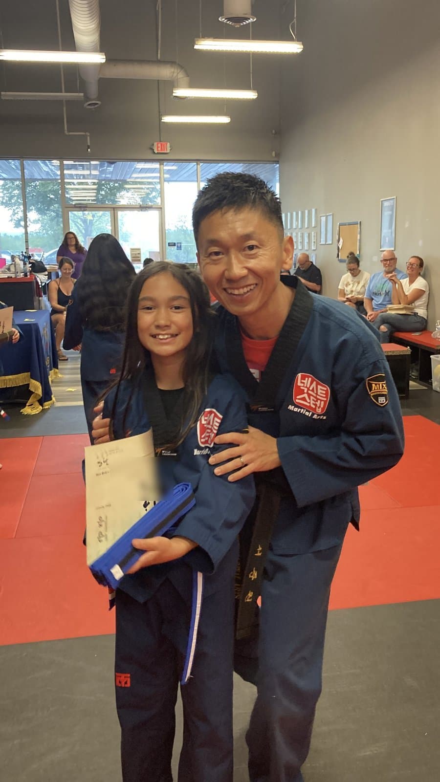A student smiling with her new belt and certificate beside Master Jay after a belt test